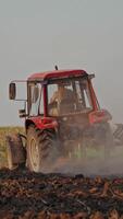 Back view of a tractor plowing the soil. Agricultural machinery preparing land for further works on the field. Process of cultivation the ground. Vertical video
