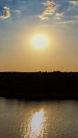 Beautiful evening view on the river at sunset. Golden path in the water from the setting sun on the natural landscape background. Aerial view. Motion camera back. Vertical video