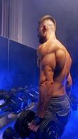 Handsome man doing exercise. Muscular man working out in gym doing exercises with dumbbells. Vertical video