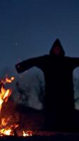 Concept of Halloween and witchcraft. Black witch in a mantle stays in front of fire. Vertical video