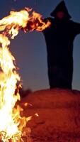 Terrible witch in the forest. Witch raising hand up near fire in forest. Vertical video