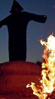 Scary figure in black mantle. Close up of witch stay around the fire in forest. Vertical video