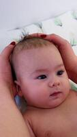Pediatrician's hands examining baby boy's head. Infant child enjoys the check-up and stares at the doctor intently. Close up. Vertical video