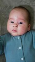 Little boy looks surprised staring into camera. Portrait of a beautiful child lying on bed close up. Grey backdrop. Vertical video