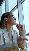 Thoughtful young female sitting at the desk in front of laptop. Woman looks into the window dreamingly and then on the computer screen. Low angle view. Vertical video