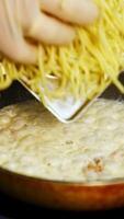 Man in white gloves puts spaghetti on a pan with white sauce. Bechamel in frying pan with pasta. Delicious dish . Vertical video
