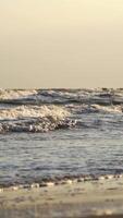 Wave drops at the beach. Close up view of sea water waves with bubbles on sand beach Vertical video