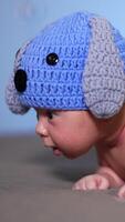 Little infant lying on his belly on the bed. Toddler just beginning to hold his head up. Small kid in a funny knitted hat with ears and diaper with tail. Vertical video