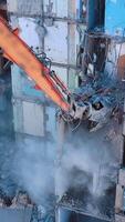 Demolition machine is breaking the floors into pieces and throwing them down. Powerful claw of excavator demolishing the ruined building. Vertical video