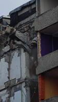Bulldozer claw grab the concrete wall in order to break it. Demolishing the building wrecked by an earthquake. View from below. Vertical video