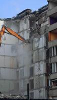Compact orange demolishing machine dismantling the house. Deconstruction of a building ruined by the nature disaster. View from below. Vertical video