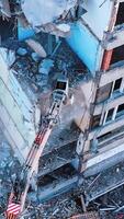 Demolishing vehicle breaks and throws down the parts of ruined house. Dismantling the old building with the help of machinery. View from above. Vertical video