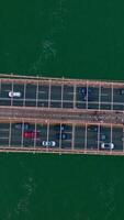 Many cars moving back and forth along the huge bridge over the river. Bird's eye view on the bridge at the backdrop of sea-green water. Vertical video