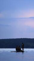 Trois Hommes voile dans une catamaran sur le rivière dans été. les mecs dans nager les troncs seul, flottant dans une pédale bateau sur une magnifique Naturel Contexte dans le soir. verticale video