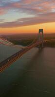 Light of setting sun falling on the supports of Whitestone bridge. Beautiful scenery of the river and Bronx at pink sky backdrop. Vertical video