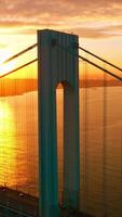 Whitestone bridge in the rays of setting sun. Cars going along the bridge back and forth. Yachts and boats sailing along the East River. Vertical video