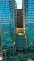 Blue skies and turquoise waters reflecting in the mirror windows of skyscrapers. Multi-line road with busy traffic near the buildings. Vertical video