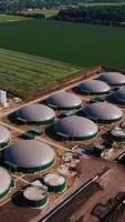 Beautiful scenery of the field containing biogas plant. Flying over the round biogas storages. Forests and village houses at the backdrop. Vertical video