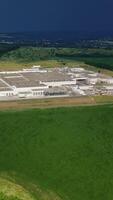 Aerial view on the large territory of industrial structure on the natural landscape in summer. Panoramic view of green fields and manufacturing buildings outdoors. Camera moves right. Vertical video