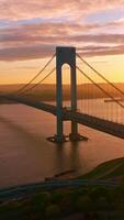 Whitestone Bridge over East River at setting sun. Sun reflecting in the calm water. Non-stopping traffic of New York. Vertical video