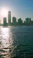 Dark silhouettes of skyscrapers at Manhattan Island. Sun reflecting in the dark water of Hudson river. Vertical video
