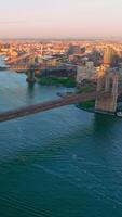 Two huge bridges crossing East river. Flying over the blue waters flowing through the fantastic New York city. Vertical video