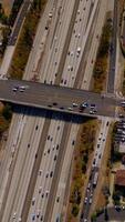 Road bridge over the wide multi-lane motorway with busy traffic. Drone descending over the freeway in Los Angeles, California, USA on sunny hot day. Vertical video