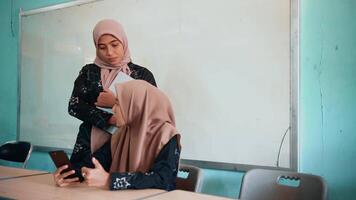 Two beautiful asian muslim women smiling happily relaxing using laptop computer, working, discussing project plans and exchanging ideas in the classroom. video