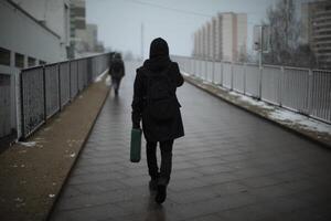 Guy carries suitcase down street.. Man in black clothes on cloudy day. photo