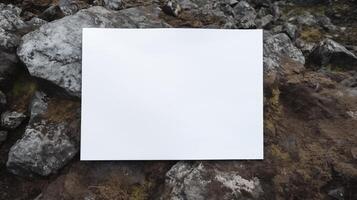 Blank white card mockup placed on uneven rocky ground with gray stones. Natural rugged environment paper template advertising image. Wilderness rocks mock up product photorealistic photo
