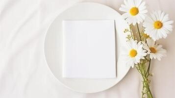 Blank card on white plate accompanied by daisies bunch on side. Camomiles flowers. Wedding invitation template advertising image. Spring chamomiles mock up product photorealistic photo