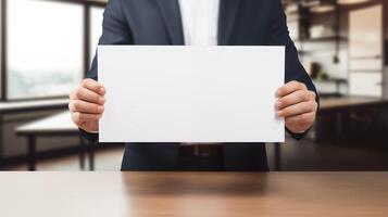 Suited man holds blank white sheet of paper above wooden desk in modern office. Empty document template advertising image. Workspace interior. Formal mock up product photorealistic photo