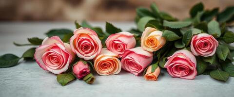 Pink and Peach Roses with Green Leaves on a White Wooden Surface photo
