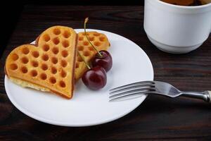 Viennese waffles with cherries lie on a white plate. Viennese waffles in the shape of a heart. photo