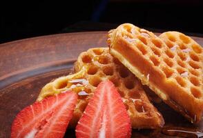 Viennese waffles drizzled with honey in the shape of a heart lie on a clay plate. Viennese waffles with cut strawberries. photo