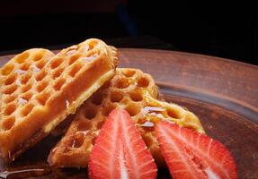 Viennese waffles drizzled with honey in the shape of a heart lie on a clay plate. Viennese waffles with cut strawberries. photo