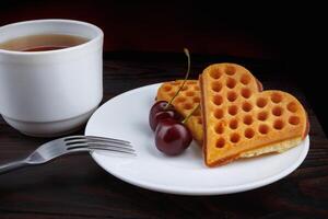Viennese waffles with cherries lie on a white plate. Viennese waffles in the shape of a heart. photo
