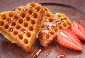 Viennese waffles drizzled with honey in the shape of a heart lie on a clay plate. Viennese waffles with cut strawberries. photo