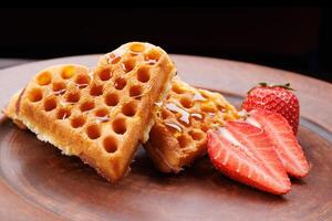 Viennese waffles drizzled with honey in the shape of a heart lie on a clay plate. Viennese waffles with cut strawberries. photo