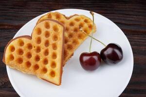 Viennese waffles with cherries lie on a white plate. Viennese waffles in the shape of a heart. photo