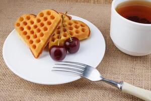 Viennese waffles with cherries lie on a white plate. Viennese waffles in the shape of a heart. photo