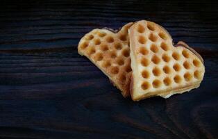 Two heart-shaped Viennese waffles lie on a dark wooden board. photo
