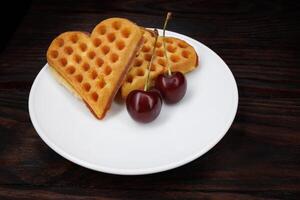 Viennese waffles with cherries lie on a white plate. Viennese waffles in the shape of a heart. photo