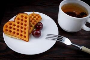Viennese waffles with cherries lie on a white plate. Viennese waffles in the shape of a heart. photo