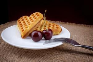 Viennese waffles with cherries lie on a white plate. Viennese waffles in the shape of a heart. photo