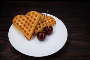 Viennese waffles with cherries lie on a white plate. Viennese waffles in the shape of a heart. photo