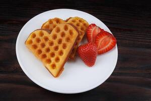 Viennese waffles with strawberries lie on a white plate. Viennese waffles in the shape of a heart. photo