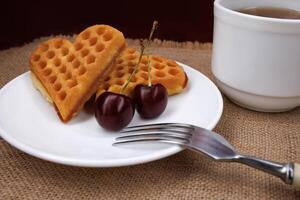 Viennese waffles with cherries lie on a white plate. Viennese waffles in the shape of a heart. photo