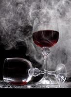 Two glasses on a black background. Smoke around a glass of wine. A glass of red wine stands on the surface, an empty glass lies next to it. photo
