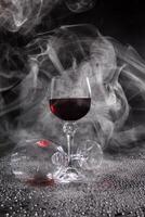 Two glasses on a black background. Smoke around a glass of wine. A glass of red wine stands on the surface, an empty glass lies next to it. photo